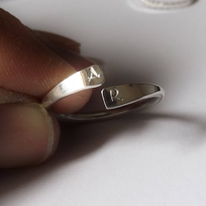 May include: A silver ring with the letters "A" and "R" engraved on it.