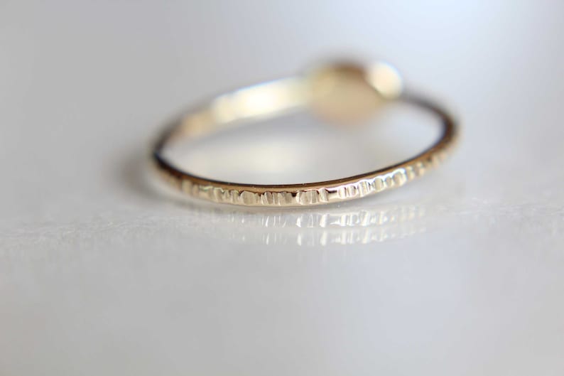 May include: A close-up of a gold ring with a textured band. The ring is on a white surface.