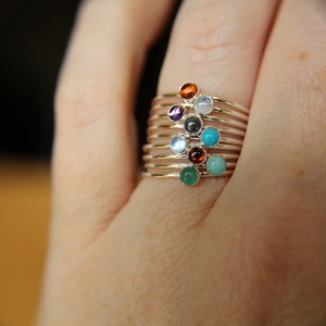 May include: A stack of delicate gold rings with colorful gemstones. The rings feature a variety of stones, including turquoise, garnet, amethyst, and moonstone.
