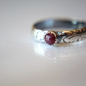 May include: A silver ring with an ornate design and a red gemstone in the center.
