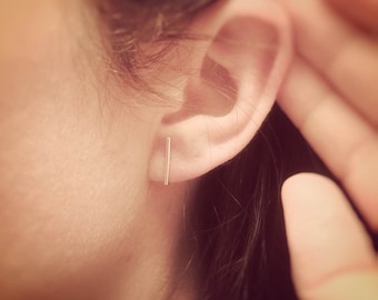Peut inclure: Gros plan sur l'oreille d'une personne avec une fine boucle d'oreille en forme de barre argentée.