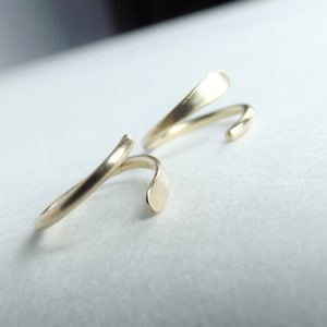 May include: Two gold-colored, twisted, open-ended rings. The rings are made of metal and have a smooth, polished finish.