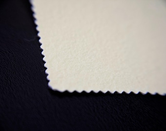 May include: A rectangular piece of off-white fabric with a textured surface and pinked edges. The fabric features a distinct zigzag pattern along its borders, creating a decorative finish on the light-colored material against a dark background.