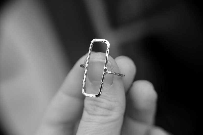 May include: A silver ring with a rectangular open frame design. The ring is textured and has a hammered finish.