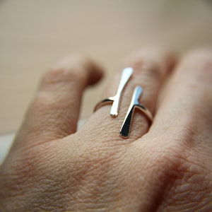May include: A silver ring with a unique, abstract design. The ring features two thin, curved lines that intersect in the center.