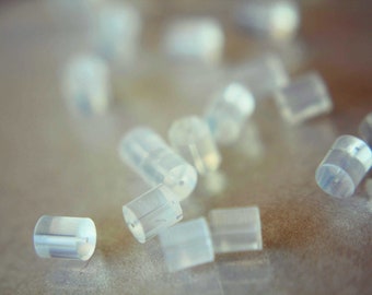 May include: A close-up of a group of small, clear, plastic earplugs scattered on a light brown surface.