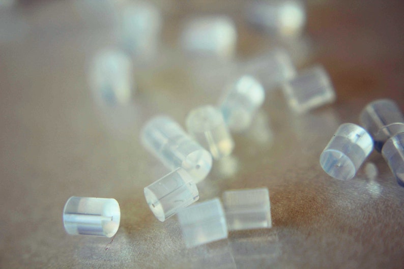 May include: A close-up of a group of small, clear, plastic earplugs scattered on a light brown surface.