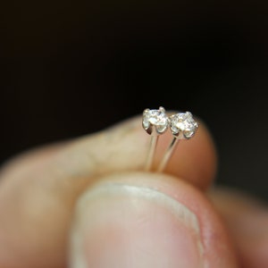 May include: A pair of silver stud earrings with small, clear gemstones.