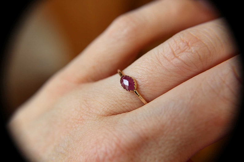 May include: A gold ring with a red oval-shaped gemstone. The ring is on a person's finger.