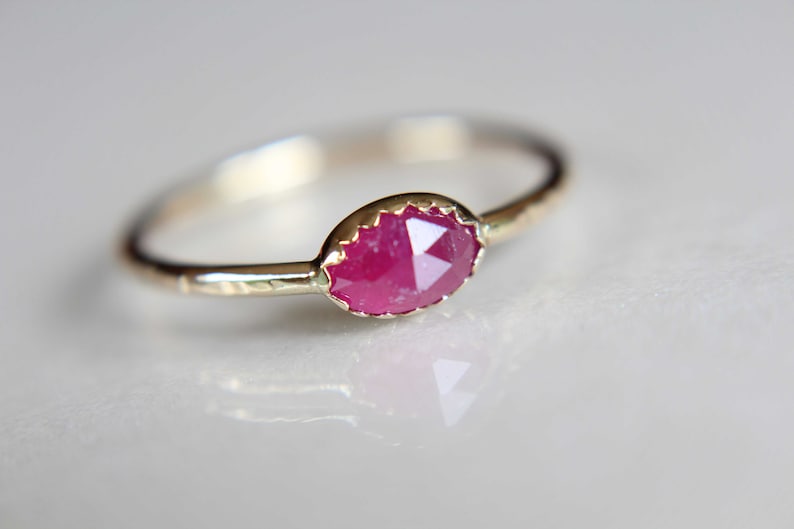 May include: A delicate gold ring with a pink ruby gemstone set in a textured band.