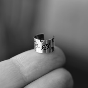 May include: A silver ear cuff with a leaf design. The cuff is open and has a curved shape.
