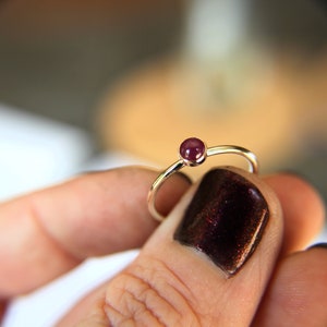 May include: A simple silver ring with a single, round, dark purple gemstone.