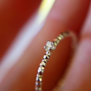 Puede incluir: Un delicado anillo de plata con un solo diamante peque&ntilde;o y transparente engastado en el centro. La banda est&aacute; texturizada con una serie de peque&ntilde;os bultos en relieve.