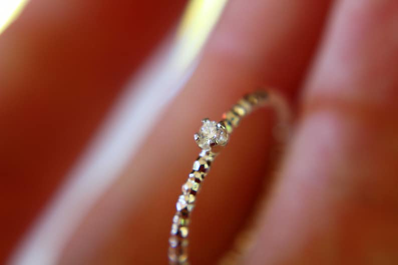 Puede incluir: Un delicado anillo de plata con un solo diamante peque&ntilde;o y transparente engastado en el centro. La banda est&aacute; texturizada con una serie de peque&ntilde;os bultos en relieve.