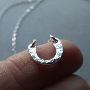 May include: A silver horseshoe pendant necklace with a hammered texture. The pendant is on a silver chain.