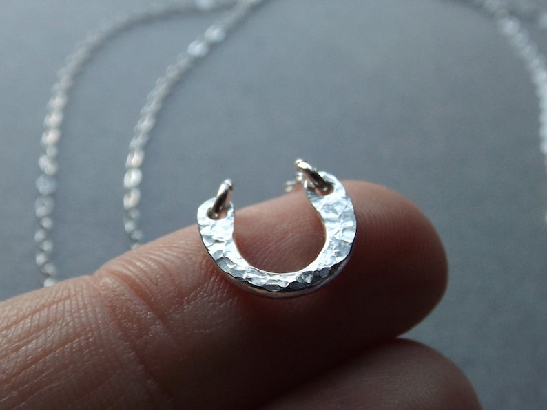 May include: A silver horseshoe pendant necklace with a hammered texture. The pendant is on a silver chain.