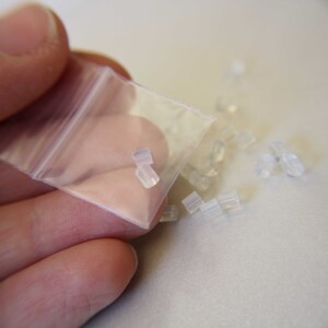 May include: A small clear plastic bag filled with clear silicone earbud tips. The bag is being held open by a hand.