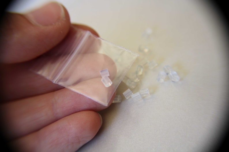 May include: A small clear plastic bag filled with clear silicone earbud tips. The bag is being held open by a hand.