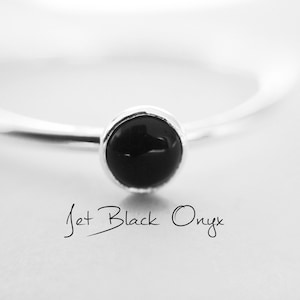 May include: A silver ring with a black jet onyx stone. The ring is on a white surface. "Jet Black Onyx" is written below the ring.