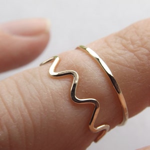May include: Two gold rings on a finger. One ring is a simple band, the other is a wavy band.