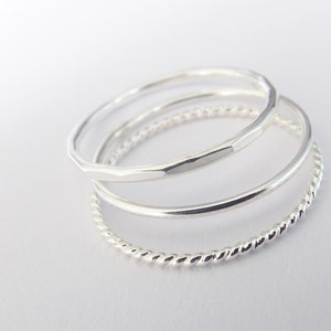 K&ouml;nnte beinhalten: Drei silberne Ringe, die &uuml;bereinander gestapelt sind. Der obere Ring ist ein geh&auml;mmertes Band, der mittlere Ring ist ein glattes Band und der untere Ring ist ein gedrehtes Band.