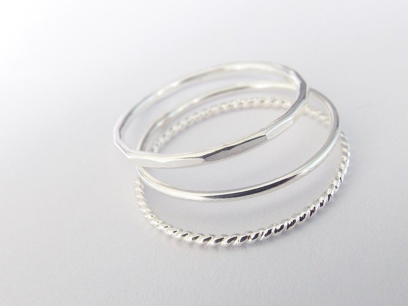 K&ouml;nnte beinhalten: Drei silberne Ringe, die &uuml;bereinander gestapelt sind. Der obere Ring ist ein geh&auml;mmertes Band, der mittlere Ring ist ein glattes Band und der untere Ring ist ein gedrehtes Band.