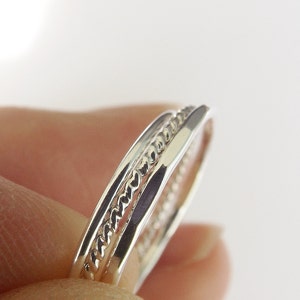 K&ouml;nnte beinhalten: Zwei silberne Ringe, einer mit einem geflochtenen Design, sind &uuml;bereinander gestapelt.