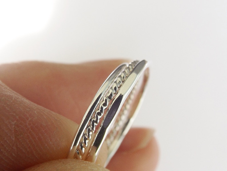 K&ouml;nnte beinhalten: Zwei silberne Ringe, einer mit einem geflochtenen Design, sind &uuml;bereinander gestapelt.
