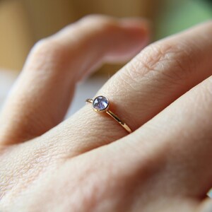 Puede incluir: Un delicado anillo de oro con una peque&ntilde;a piedra preciosa redonda de color p&uacute;rpura engastada en el centro.