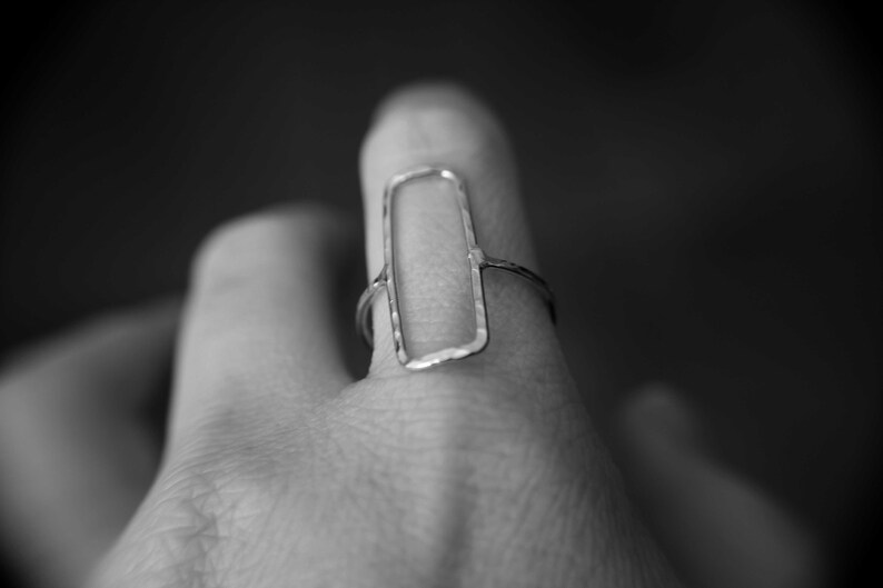May include: A silver ring with a rectangular, open-work design. The ring is worn on a person's finger.