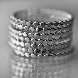 May include: A stack of silver rings with a textured, circular design. Each ring is made of small, connected circles.