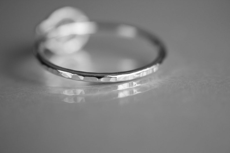 K&ouml;nnte beinhalten: Ein silberner Ring mit geh&auml;mmerter Textur. Der Ring liegt auf einer grauen Oberfl&auml;che.