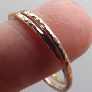 May include: Two thin gold rings with a hammered texture, worn on a finger.