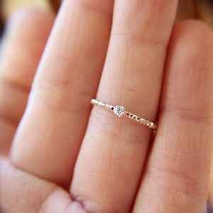 Puede incluir: Un delicado anillo de plata con una peque&ntilde;a piedra preciosa transparente engastada en el centro. El anillo es fino y tiene un dise&ntilde;o de cuentas.