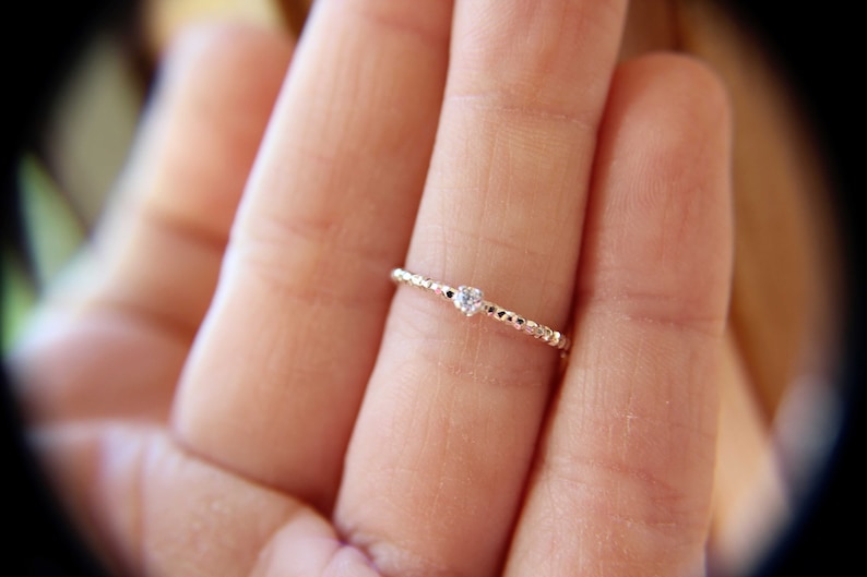 Puede incluir: Un delicado anillo de plata con una peque&ntilde;a piedra preciosa transparente engastada en el centro. El anillo es fino y tiene un dise&ntilde;o de cuentas.