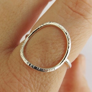 Puede incluir: Un anillo de plata con una banda texturizada de forma ovalada. El anillo se lleva en un dedo.