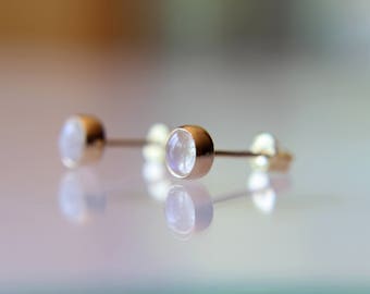Puede incluir: Un par de pendientes de botón de oro con piedras de luna redondas y blancas.