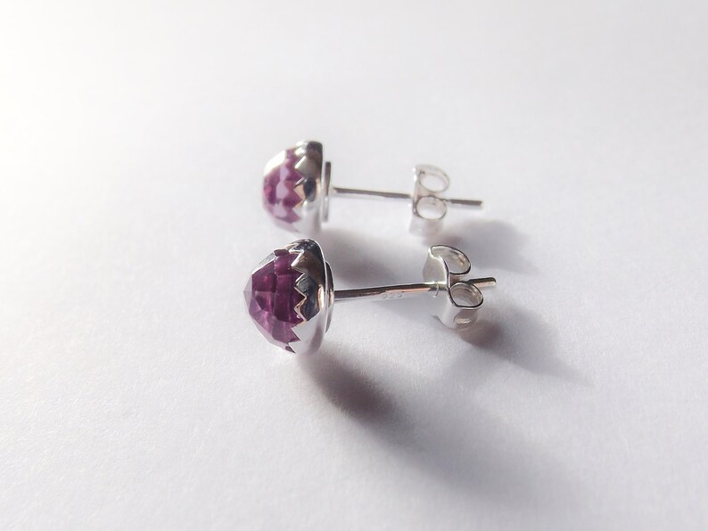 Peut inclure: Une paire de boucles d'oreilles en argent avec une pierre pr&eacute;cieuse violette au centre de chaque boucle d'oreille.