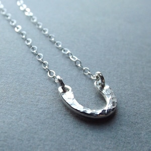 May include: A silver necklace with a hammered horseshoe pendant. The chain is delicate and the pendant is small.