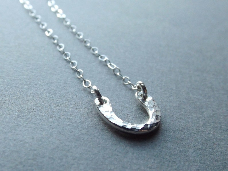 May include: A silver necklace with a hammered horseshoe pendant. The chain is delicate and the pendant is small.