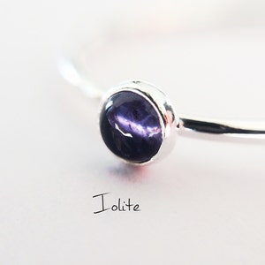 May include: A silver ring with a round, dark purple iolite gemstone. The ring is simple and elegant.