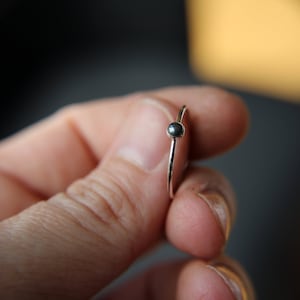 May include: A silver ring with a small, dark grey gemstone.