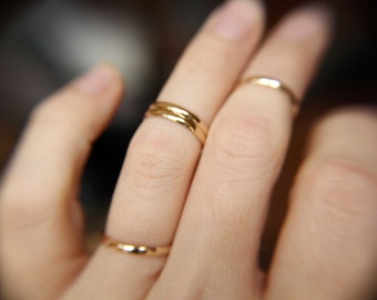 May include: A hand wearing three gold rings on the ring finger.