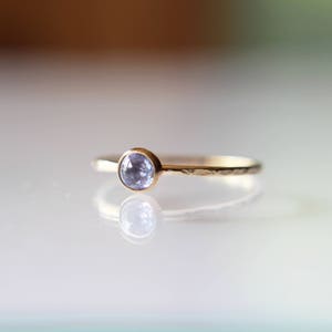 Puede incluir: Un delicado anillo de oro con una banda martillada y una peque&ntilde;a piedra preciosa redonda de color azul claro.