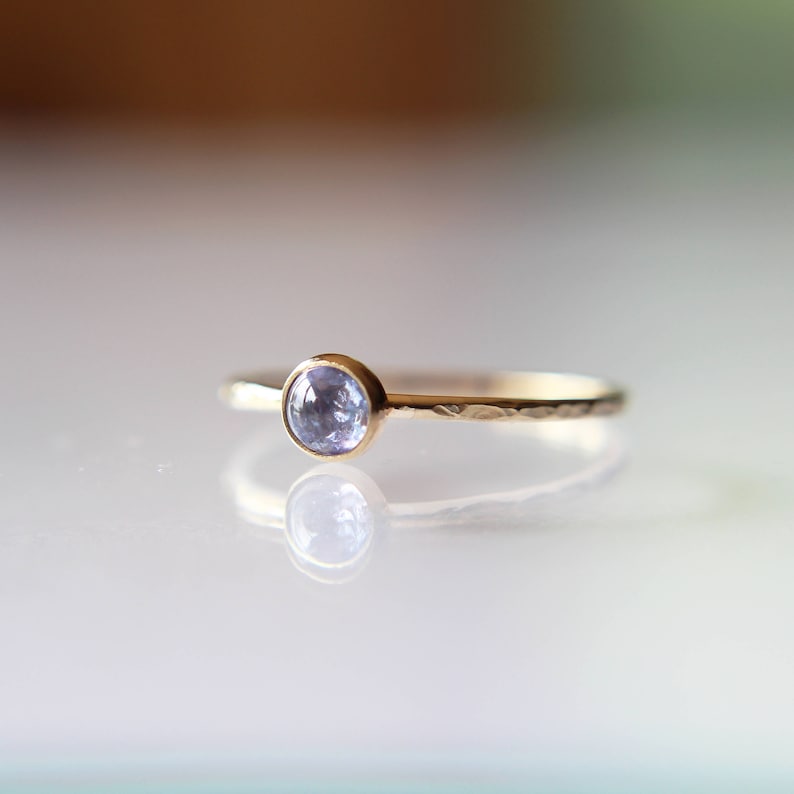 Puede incluir: Un delicado anillo de oro con una banda martillada y una peque&ntilde;a piedra preciosa redonda de color azul claro.