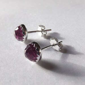 Peut inclure: Une paire de boucles d'oreilles en argent avec des pierres pr&eacute;cieuses violettes. Les pierres pr&eacute;cieuses sont facett&eacute;es et ont une forme l&eacute;g&egrave;rement arrondie.