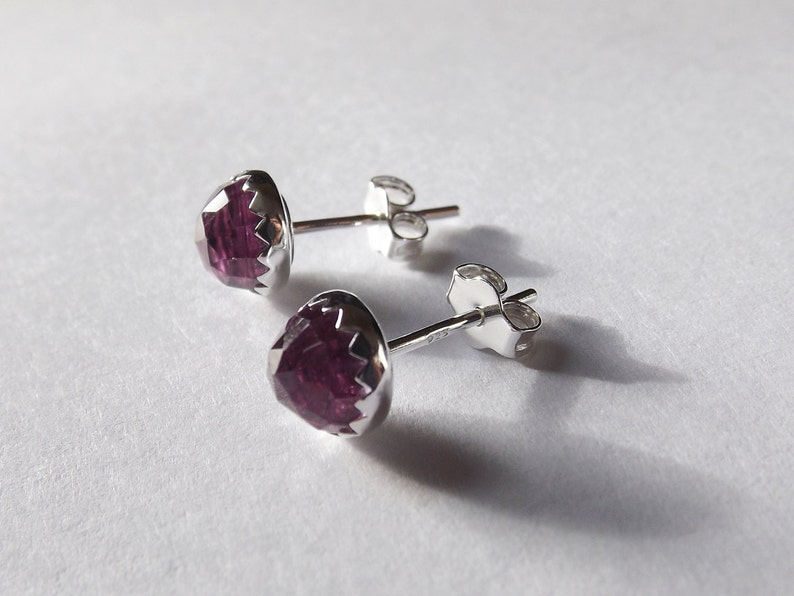 Peut inclure: Une paire de boucles d'oreilles en argent avec des pierres pr&eacute;cieuses violettes. Les pierres pr&eacute;cieuses sont facett&eacute;es et ont une forme l&eacute;g&egrave;rement arrondie.
