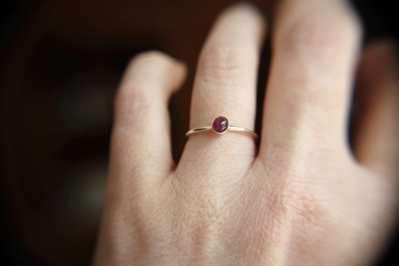 Peut inclure: Une bague simple en or avec une petite pierre pr&eacute;cieuse ronde de couleur rouge fonc&eacute;.