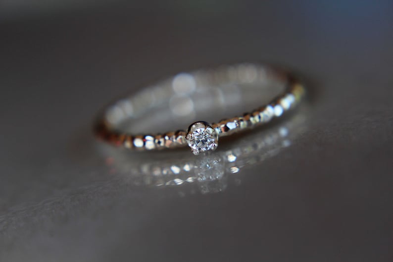 Puede incluir: Un anillo de plata con un peque&ntilde;o diamante transparente engastado en el centro. La banda est&aacute; texturizada con peque&ntilde;as cuentas.