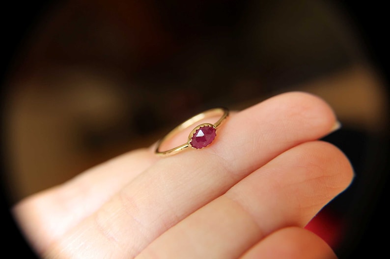 May include: A gold ring with a red gemstone set in the center. The ring is on a person's finger.